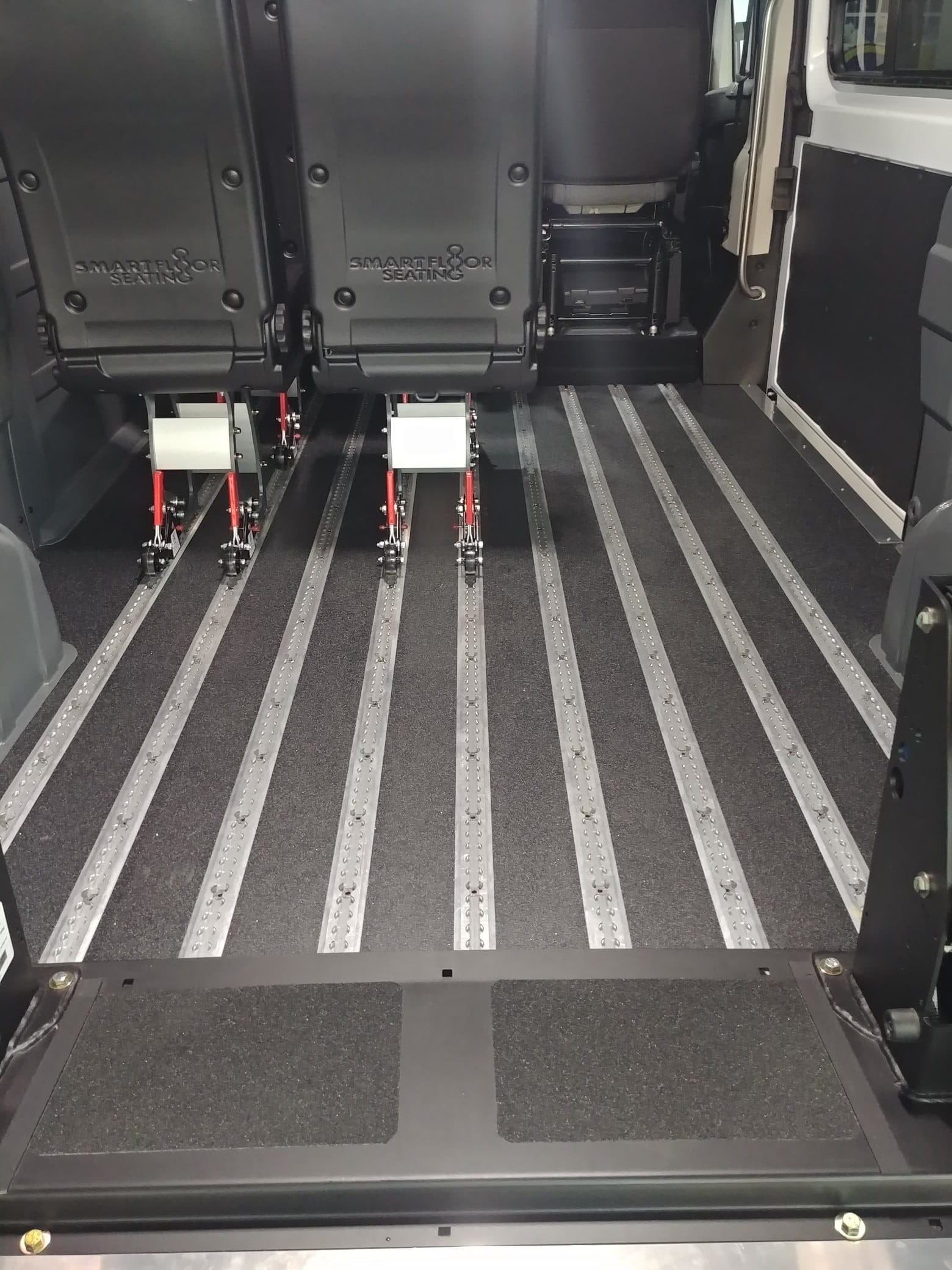 The ProMaster floor from the open rear doors: full length aluminium securement tracks running the length of the van, with two quick-release seats mounted on them and the rest of the floor left clear