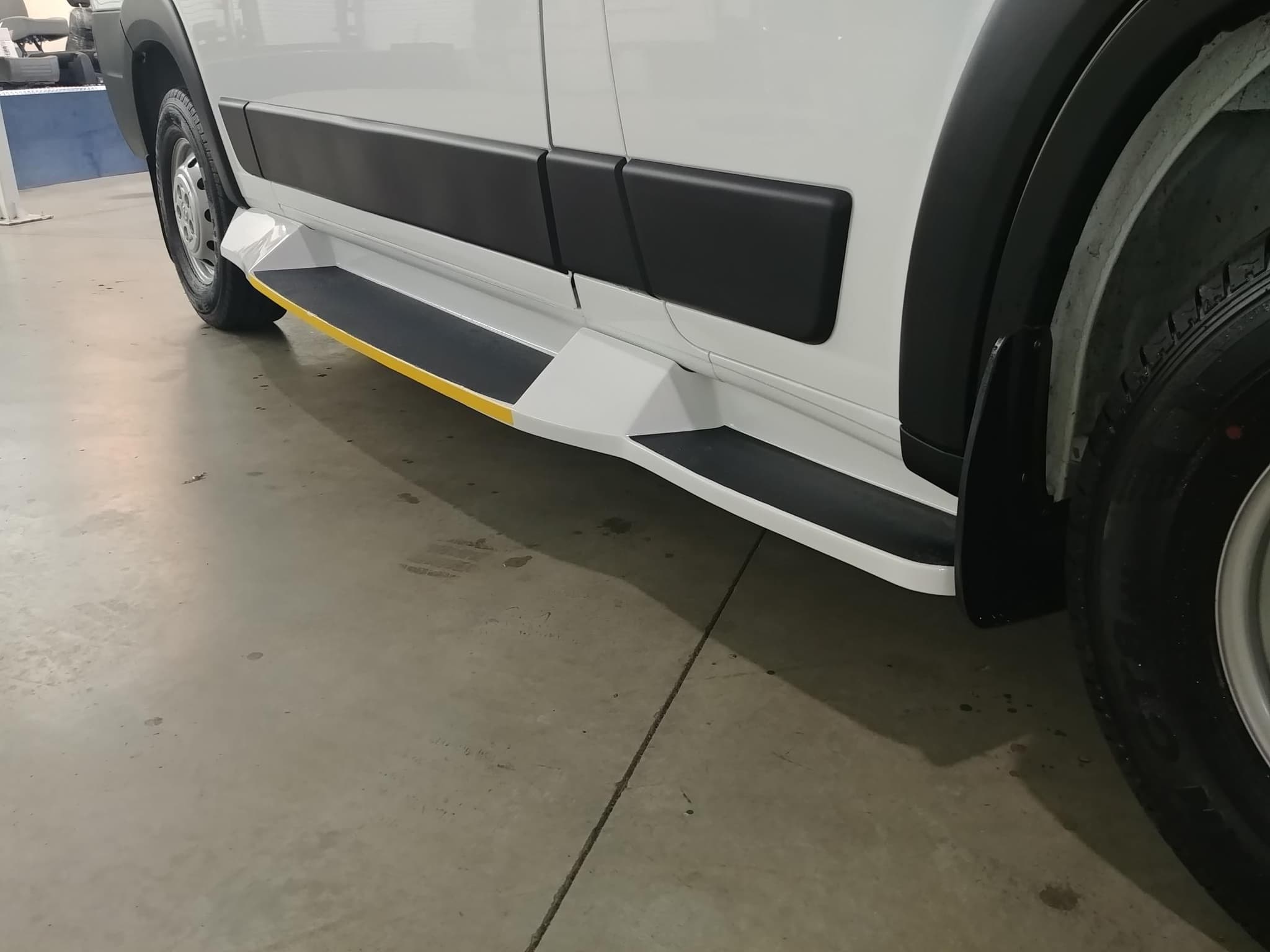 Close view of the white powder-coated entry step fitted along the side of the ProMaster, with a black non-slip tread surface and a yellow high-visibility edge