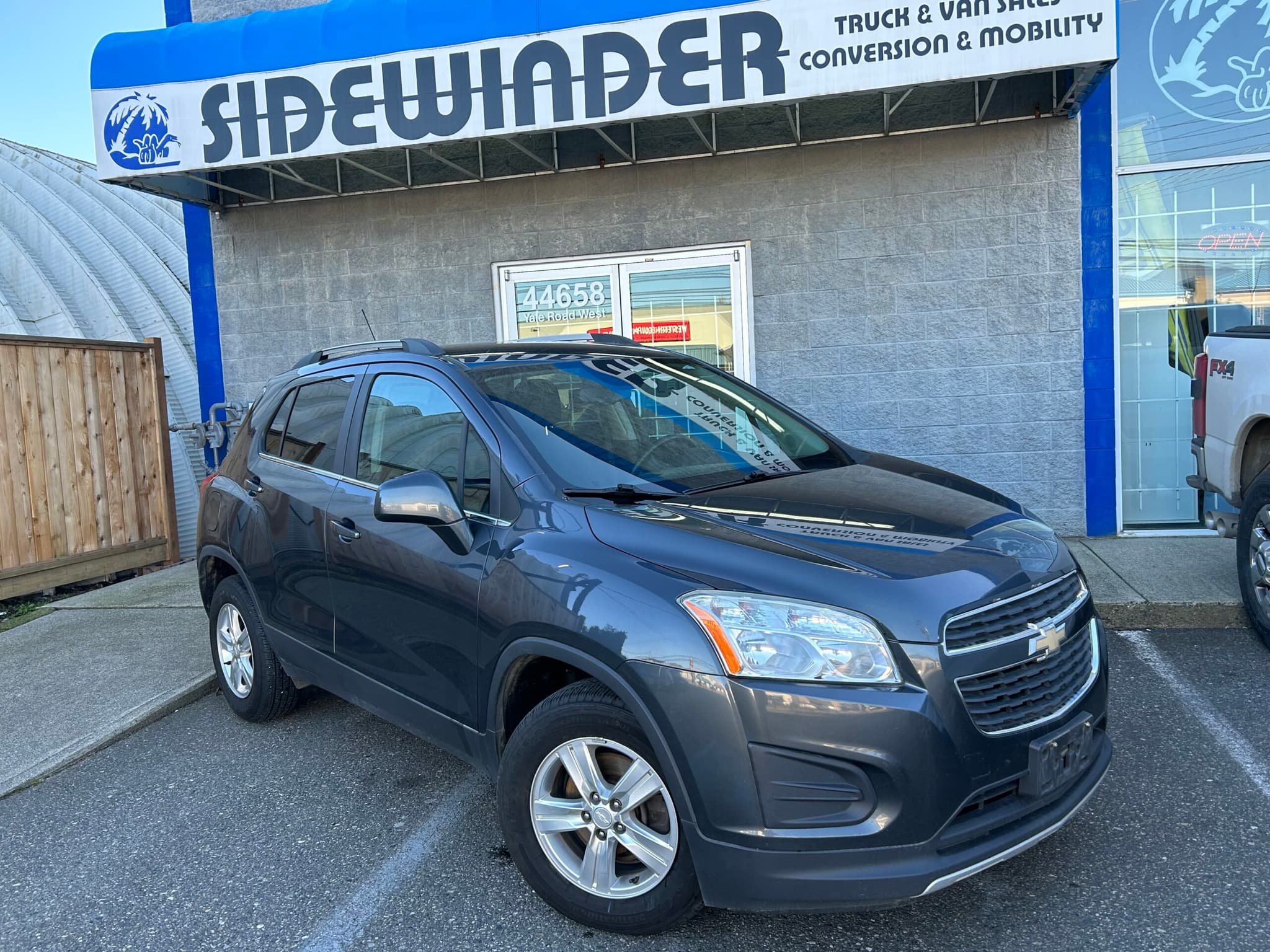Dark grey Chevrolet Trax LT parked under the Sidewinder Truck & Van Sales sign at 44658 Yale Road West in Chilliwack, front three-quarter view