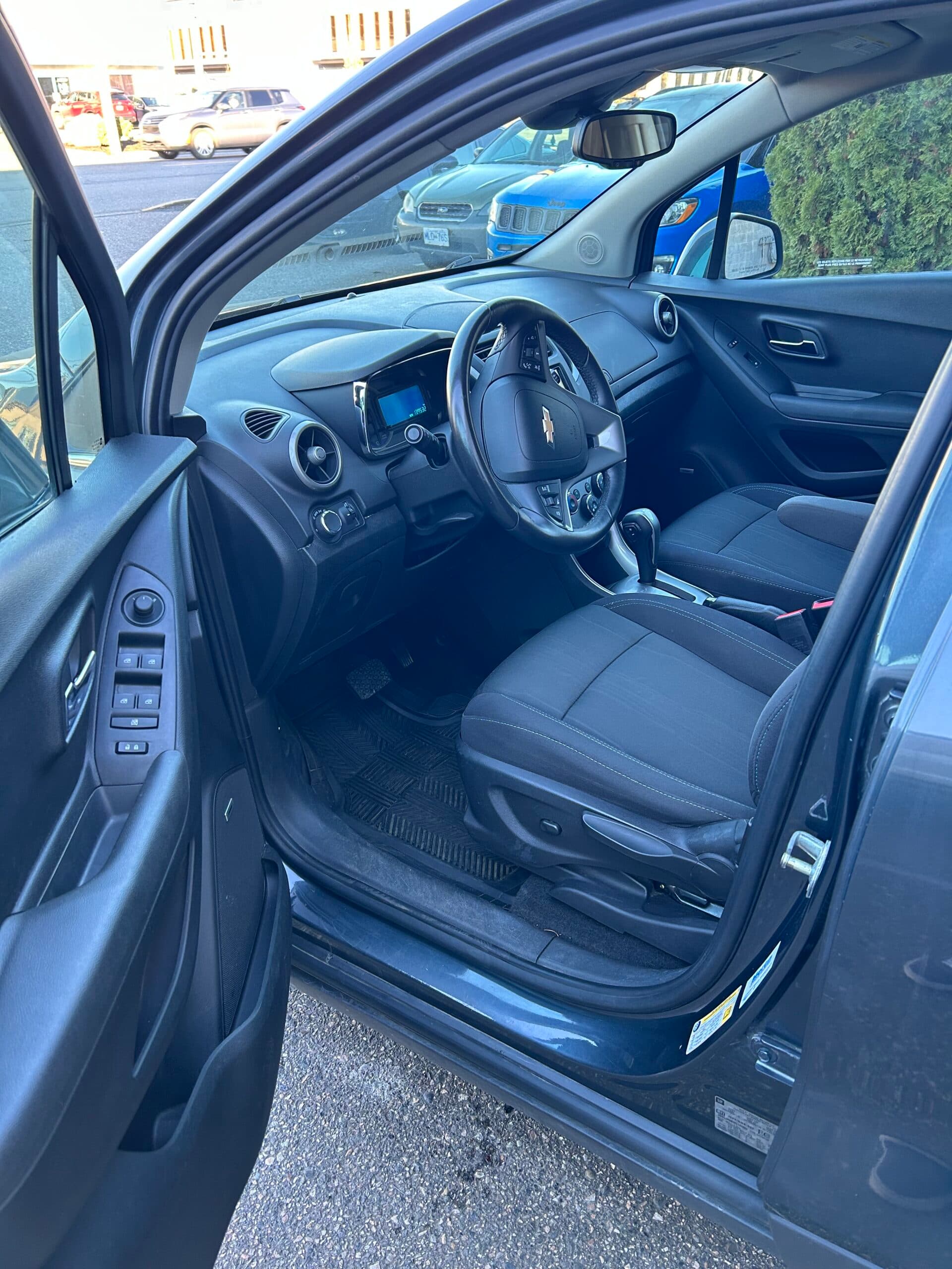Driver's seat and door of the Trax from outside, black cloth upholstery with power window and mirror controls on the door panel
