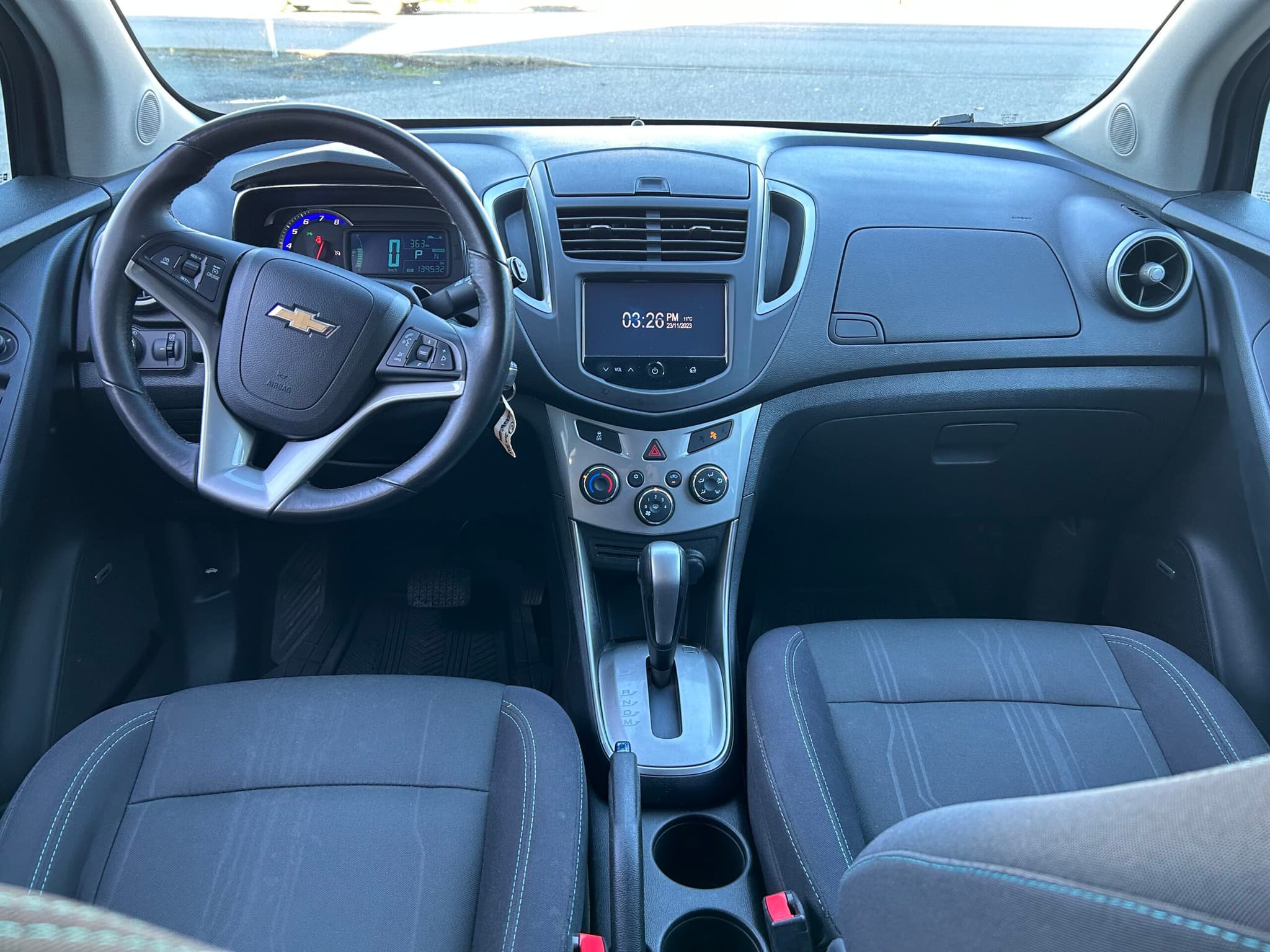 Dashboard of the Trax from the rear seat: leather-wrapped steering wheel with audio controls, colour touchscreen, automatic shifter and black cloth front seats