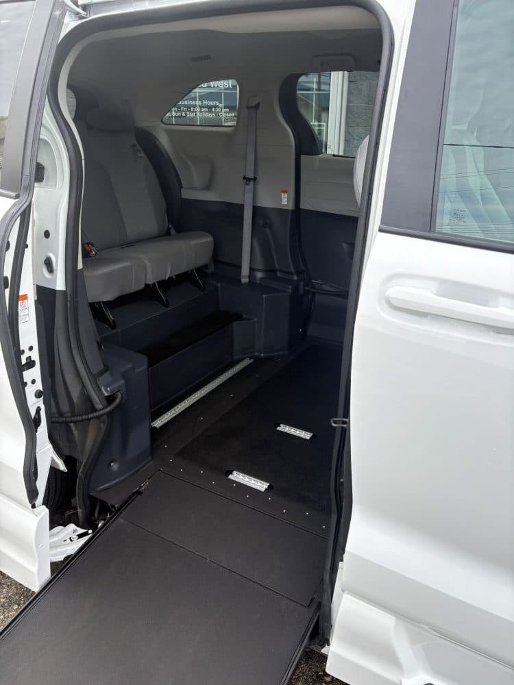 Looking into the same Sienna through the open side door: the lowered floor sits level with the deployed ramp, with securement tracks set flush into the floor and a grey bench seat behind