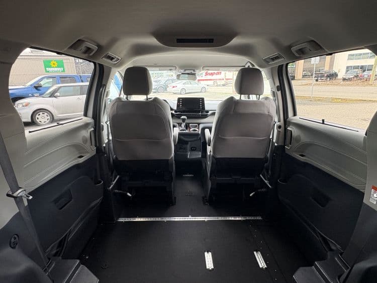 Interior of the Sienna from the rear, looking forward past the two grey cloth front seats over an open flat lowered floor with a securement track running down the centre