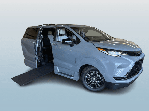 Grey Toyota Sienna XSE with the sliding side door open and the VMI Northstar in-floor ramp deployed to the ground, front three-quarter view on black alloy wheels, photographed against a plain background