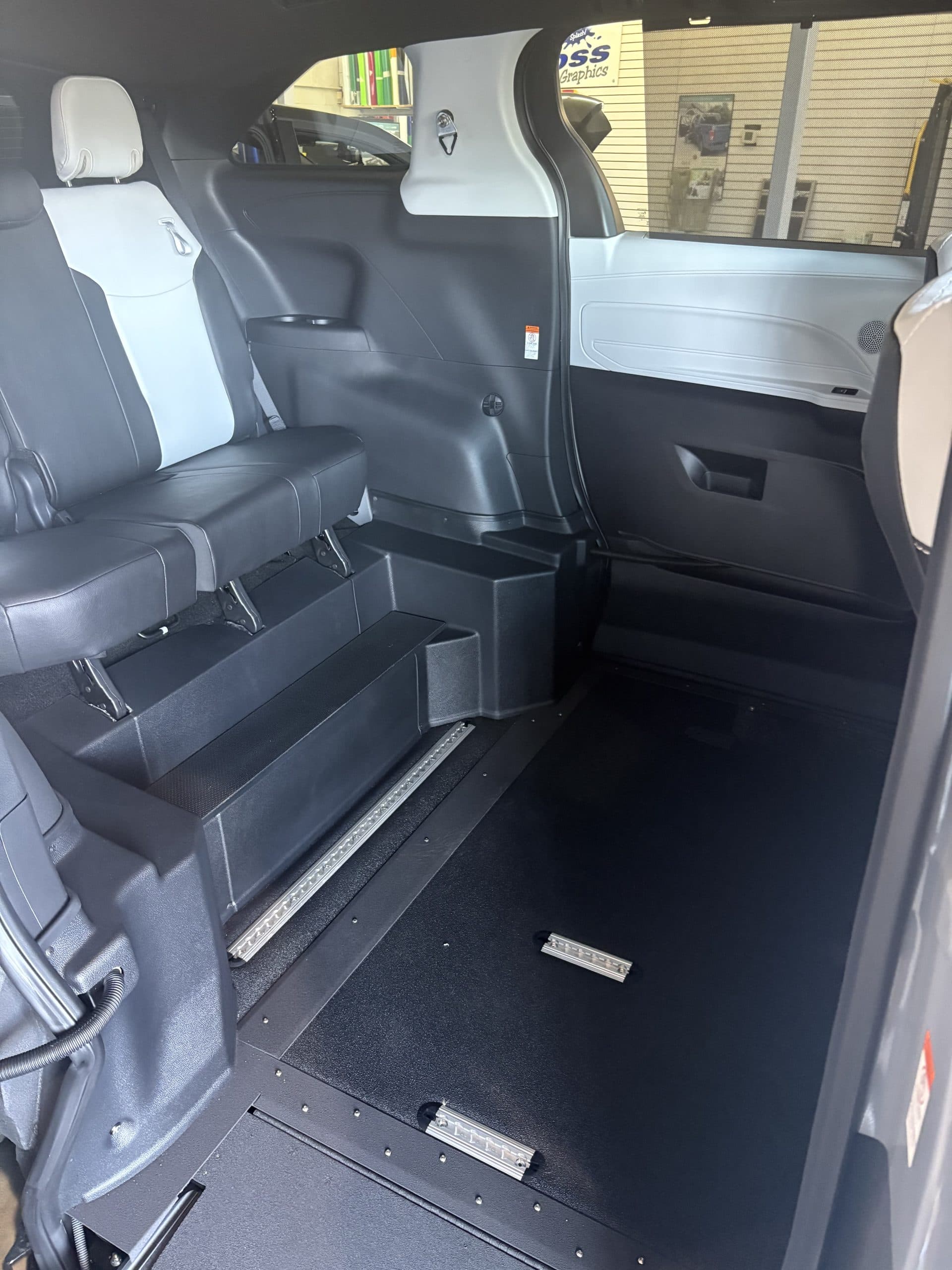 Inside the Sienna through the open side door: the lowered floor with securement tracks set flush into it, a black and light grey second row bench, and the wheel well covers moulded into the side panels