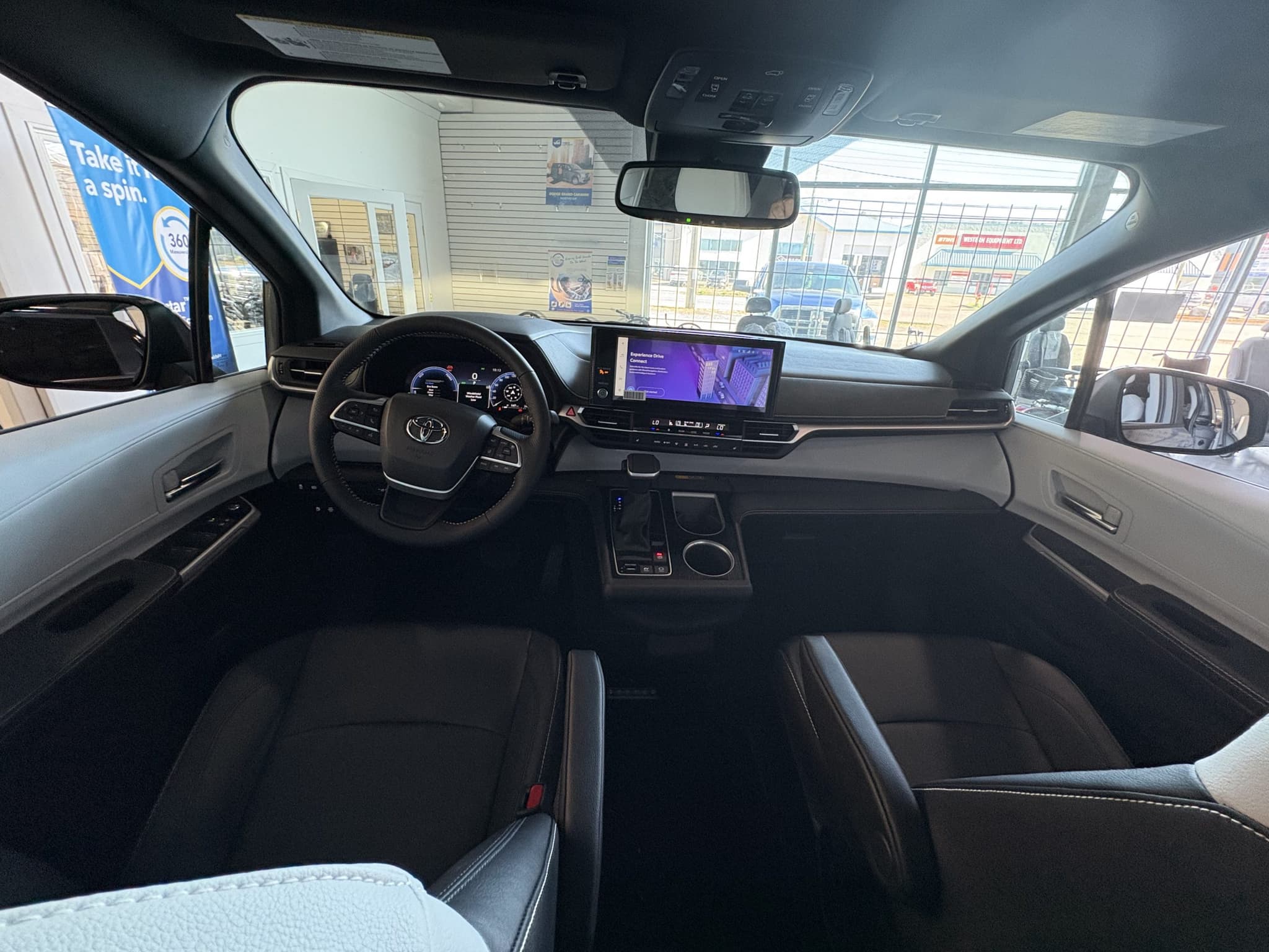 Front cabin of the Sienna seen from the second row: Toyota steering wheel, digital instrument cluster and a wide central touchscreen, with black and light grey two-tone trim