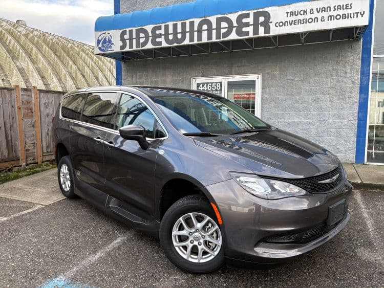 The same granite grey Grand Caravan parked outside the Sidewinder Truck & Van Sales storefront on Yale Road West in Chilliwack, doors closed, front three-quarter view