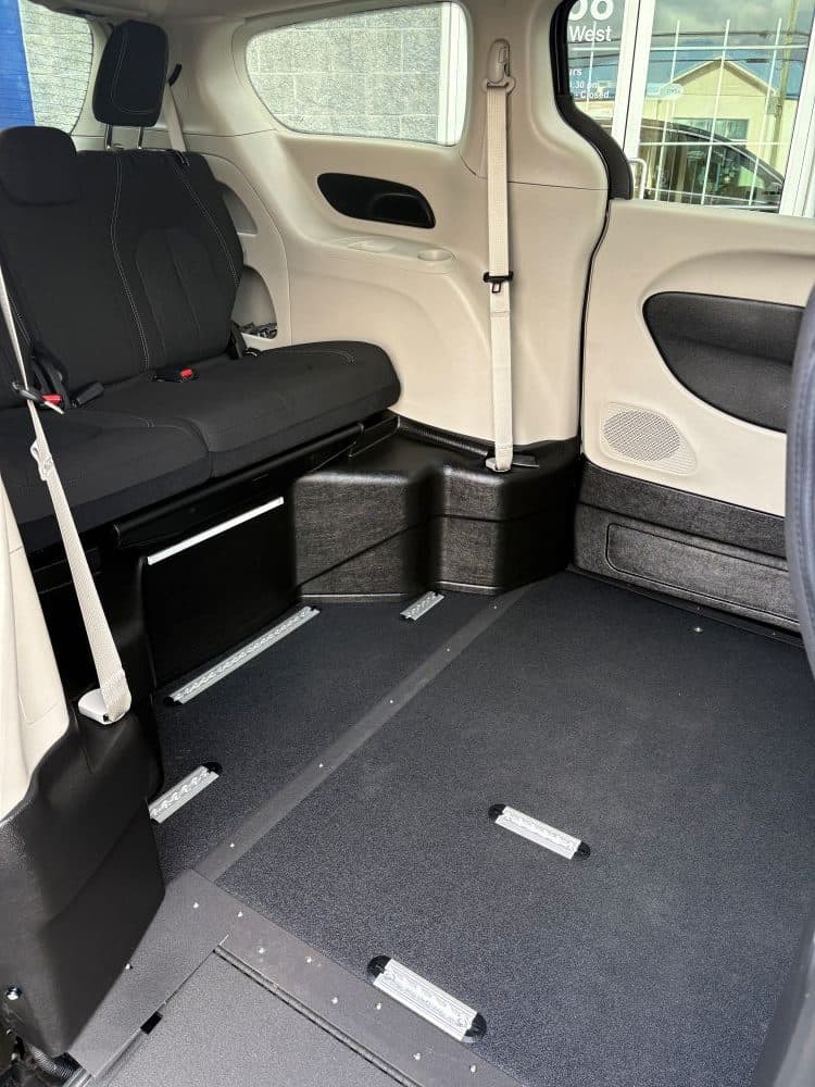 Looking in through the open side door: the lowered floor finished in black non-slip flooring with securement tracks set into it, a black second row bench folded to the side, and beige interior panels