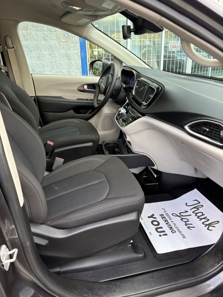 Driver's seat and dashboard from the open driver's door, black cloth upholstery, with a Sidewinder thank-you mat laid in the footwell