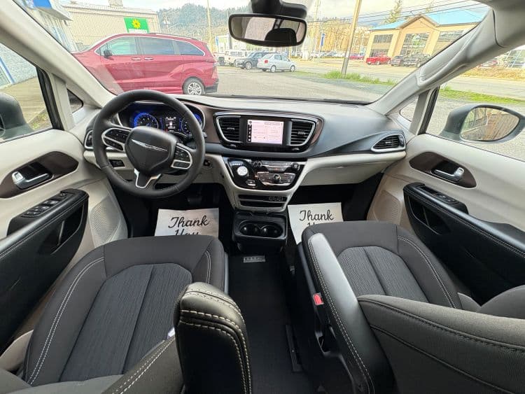 Front cabin seen from the second row: Chrysler steering wheel, central touchscreen and climate controls, with black cloth front seats and beige upper trim